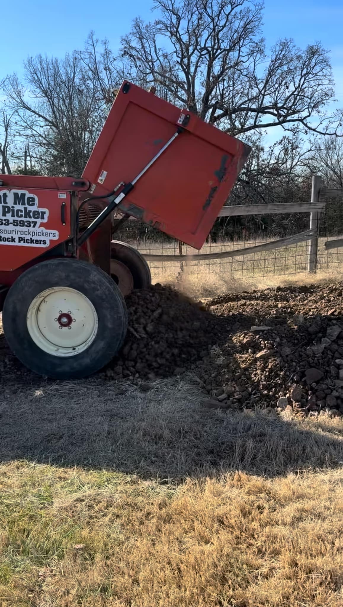 Portion of a red machine that appears to be dumping a load of material on the ground. 